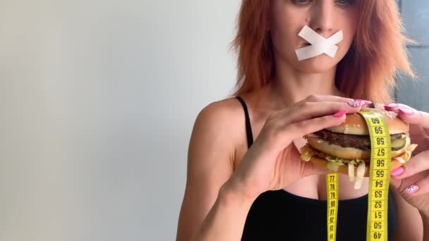 Dieet. Portret van een vrouw wil een hamburger te eten, maar een gelijmde mond, een begrip van dieet, ongezond voedsel, een wil in voeding — Stockvideo