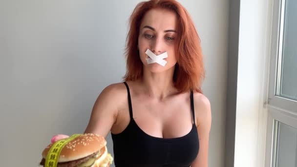 Dieta. Retrato de uma mulher quer comer um hambúrguer, mas uma boca colada, uma noção de dieta, comida insalubre, uma vontade em nutrição — Vídeo de Stock