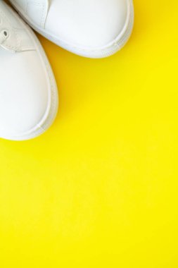 Sarı arka planda şık beyaz moda spor ayakkabıları.