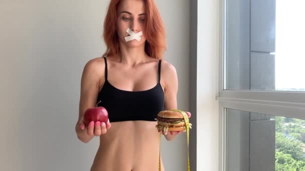 Dieet. Portret van een vrouw wil een hamburger te eten, maar een gelijmde mond, een begrip van dieet, ongezond voedsel, een wil in voeding. — Stockvideo