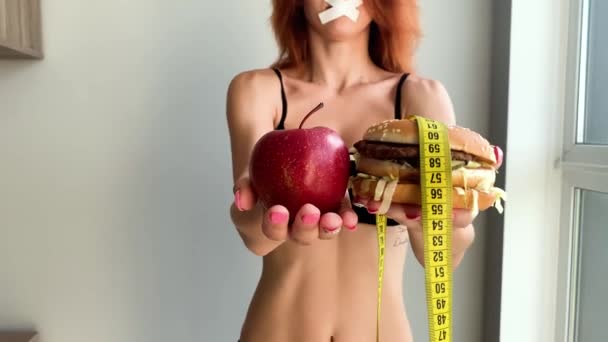 다이어트. 여자의 초상화는 햄버거를 먹고 싶어하지만, 접착 입, 다이어트의 개념, 건강에 해로운 음식, 영양의 의지. — 비디오