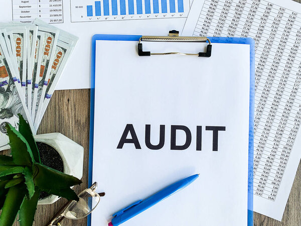 Clipboard with text audit on wood desk.