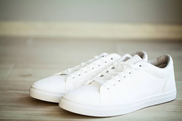 Пара новых стильных белых кроссовок на полу дома — стоковое фото