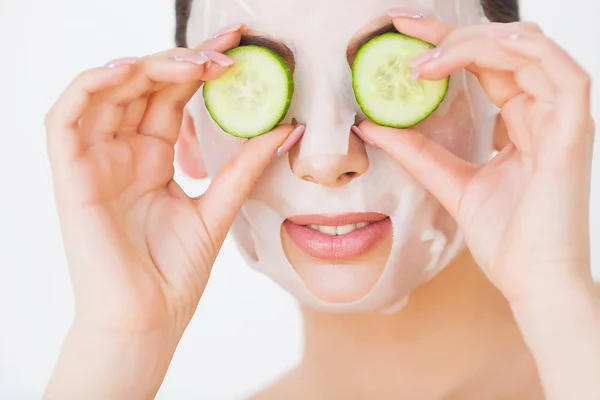 Mulher bonita em máscara de barro lama no rosto cobrindo os olhos com fatias de pepino . — Fotografia de Stock