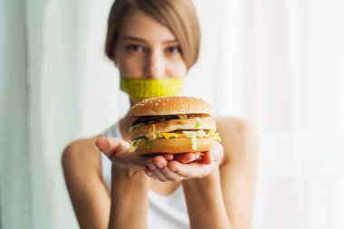 Diyet. Kadın portre bir Burger ama sıkışmış skochem ağız, diyet, abur cubur, irade beslenme kavramı yemek istiyor