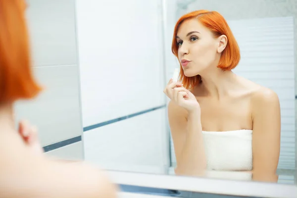 Cuidado com a pele. Mulher com cabelo vermelho fazer maquiagem no banheiro leve . — Fotografia de Stock