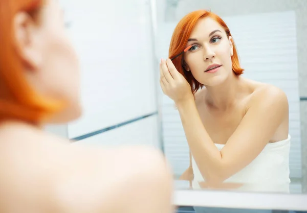 Cuidado com a pele. Mulher com cabelo vermelho fazer maquiagem no banheiro leve . — Fotografia de Stock