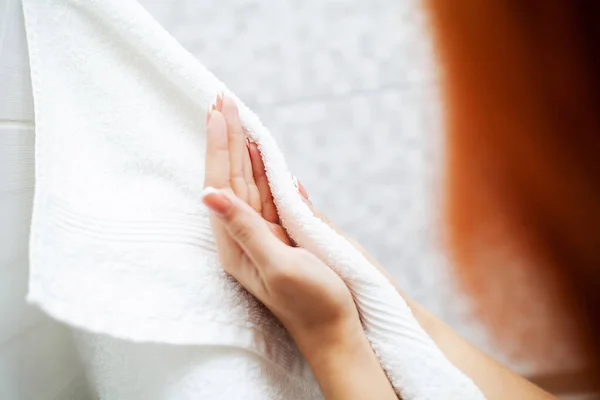 Гигиена и уход за руками. Женщина, использующая полотенце для вытирания сухих рук после мытья в светлой ванной комнате дома — стоковое фото