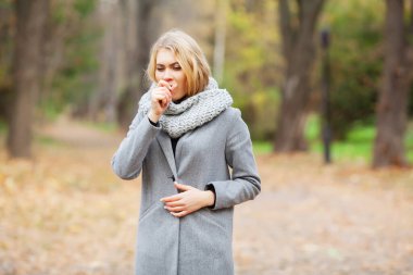 Soğuk algınlığı ve grip. Sonbahar park ve el donmuş sıcak yürüyüş gri paltolu genç kadın