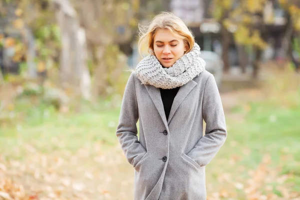 Cold and flu. Young woman in a gray coat walking in the autumn park and warms frozen hand — Stock Photo, Image