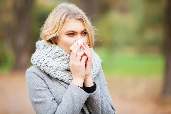 Wanita muda meniup hidungnya di taman. Perempuan potret bersin di luar ruangan karena dingin dan flu — Stok Foto
