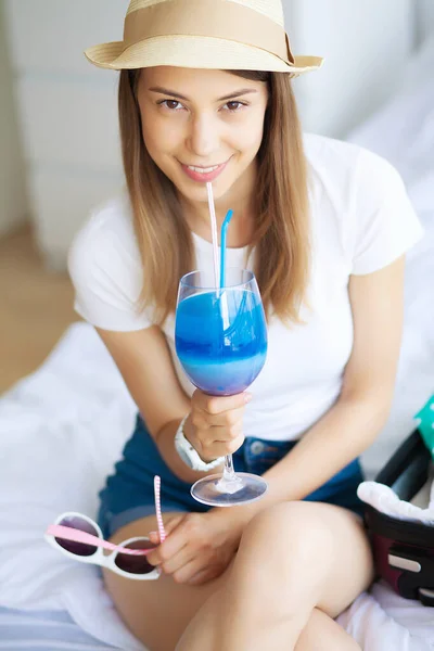 Una vacanza. Donna che si sta preparando per il riposo. Giovane bella ragazza si siede sul letto. Ritratto di donna sorridente. Felice ragazza va in vacanza — Foto Stock