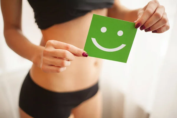 Salud de las mujeres. Primer plano de la hembra sana con hermoso ajuste cuerpo delgado en bragas negras sosteniendo tarjeta verde con la cara sonriente feliz en las manos — Foto de Stock
