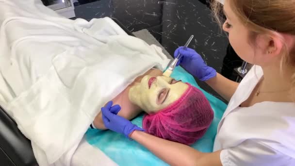 Spa therapie voor jonge vrouw gezichtsmasker gelet op de salon van de schoonheid. — Stockvideo