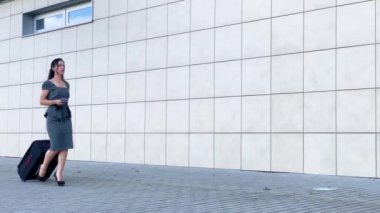 Tatil. Gülümseyen kadın yolcu havaalanı yolcu salonundan bavulçekerek kapıdan çıkışa doğru ilerliyor