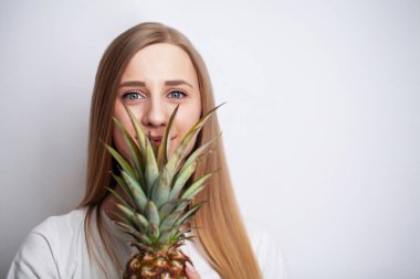 Genç bir kadın yüzünde olgun bir ananas tutuyor.