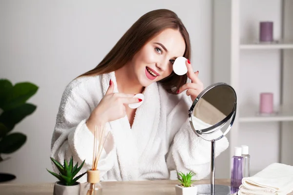 Evde genç bir kadın banyoda aynanın önünde yüzüne makyaj yapıyor. — Stok fotoğraf