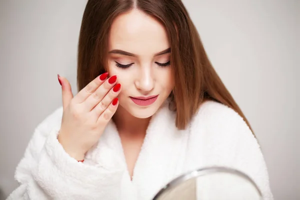 Νεαρή γυναίκα στο σπίτι βάζει μακιγιάζ στο πρόσωπο στο μπάνιο μπροστά από έναν καθρέφτη — Φωτογραφία Αρχείου