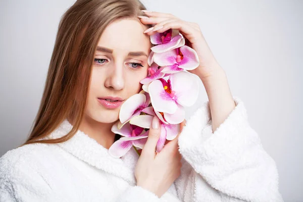 Gesichtspflege. Junge Frau mit schöner Haut hält Orchidee in der Hand — Stockfoto