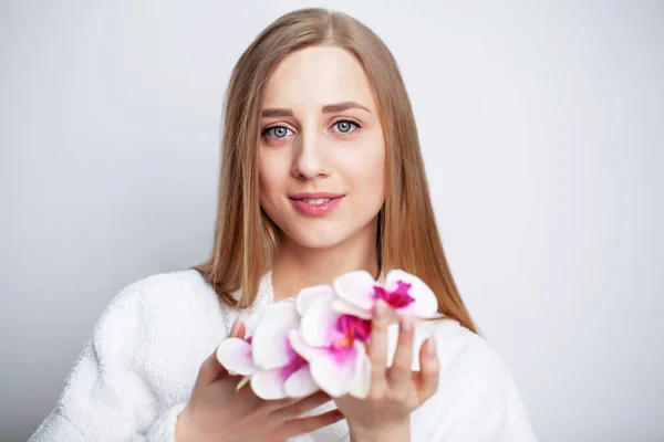 Gesichtspflege. Junge Frau mit schöner Haut hält Orchidee in der Hand — Stockfoto