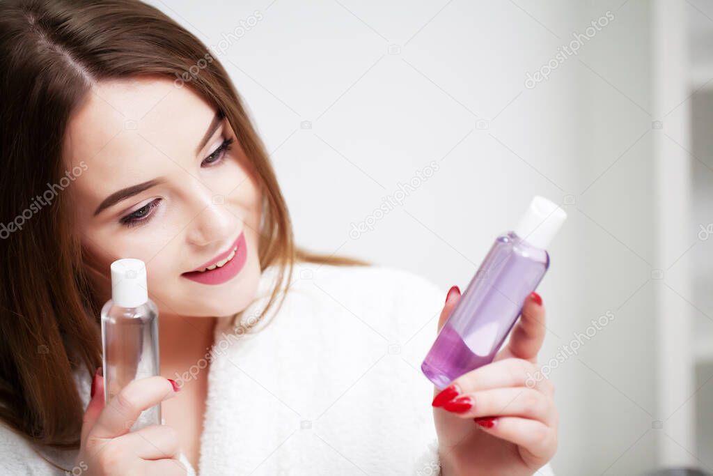 Young woman at home applies makeup on the face in the bathroom in front of a mirror