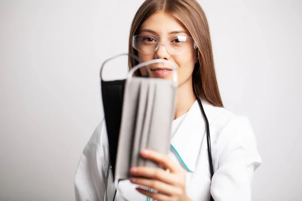 Молодая женщина-врач в очках держит защитную маску — стоковое фото