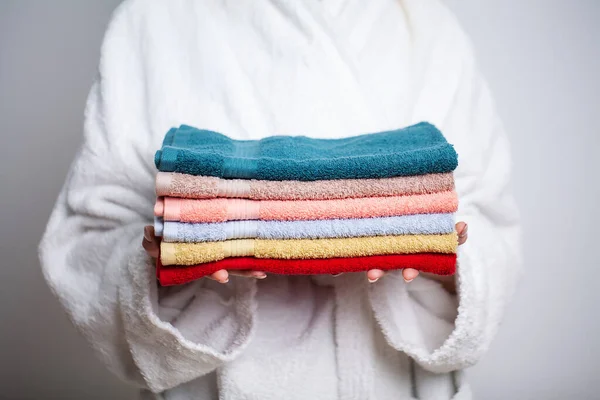 Woman in a white coat holding a stack of colored towels — Stock Photo, Image