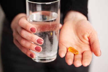 Omega 3 hapı ve bir bardak su tutan bir kadın.