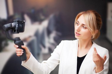 Genç iş kadını şirket ofisinde akıllı telefondan video blogu kaydediyor.