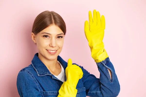 Woman cleaner in overalls and yellow gloves posing on a pink background