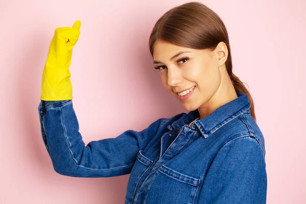 Woman cleaner in overalls and yellow gloves posing on a pink background