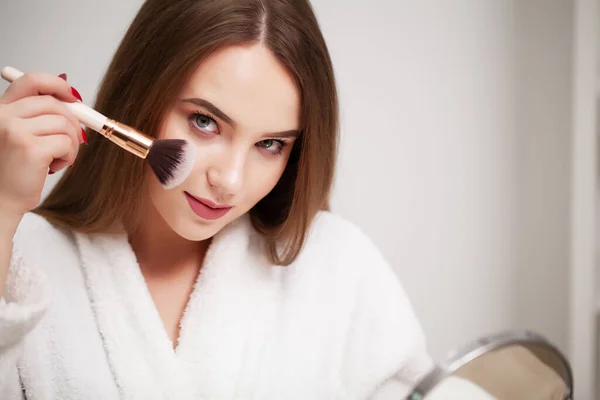 Güzellik makyajı, temiz ciltli genç bir kadın yüzüne makyaj yapmak için fırça tutuyor. — Stok fotoğraf