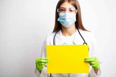 Maskeli genç bir kadın doktor boş bir kâğıt parçası tutuyor.