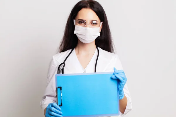 Jovem médica em uma máscara segura uma folha de papel em branco com espaço para texto — Fotografia de Stock