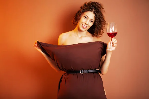 Pretty young woman taking part in a call with a pillow and holding a glass of red wine