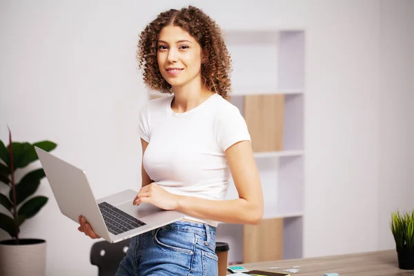 Mujer positiva feliz con rizos en la cabeza trabajando en la oficina en un ordenador portátil —  Fotos de Stock