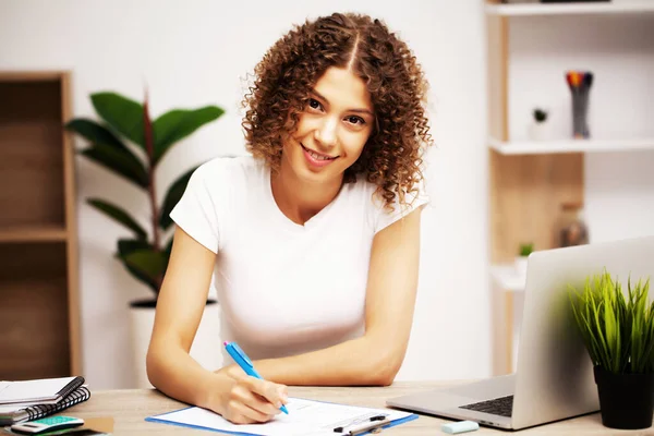 Glückliche positive Frau mit Locken auf dem Kopf, die im Büro an einem Laptop arbeitet — Stockfoto