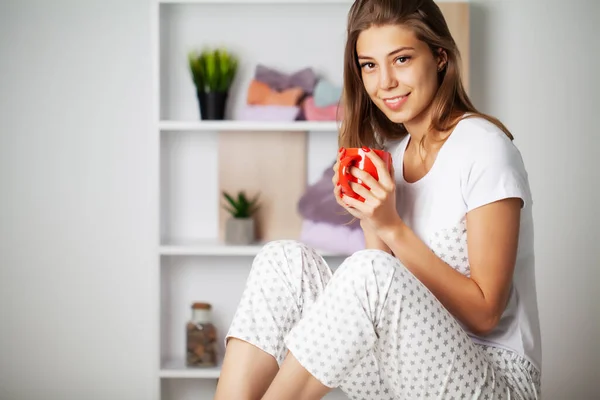 Jonge vrouw in comfortabele pyjama zitten op de tafel in haar kamer — Stockfoto