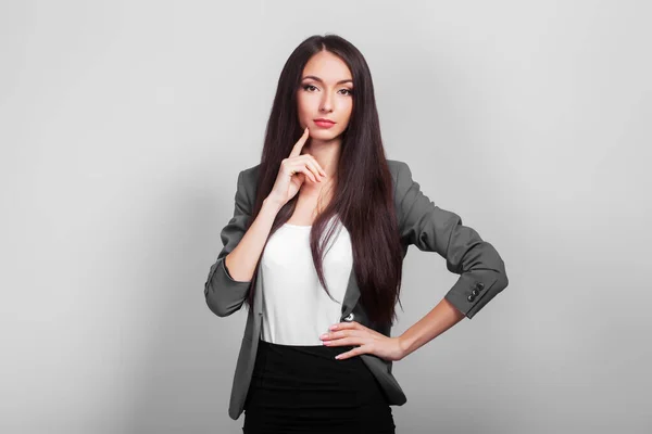 Belle femme d'affaires aux cheveux foncés, pensant debout sur un fond gris — Photo