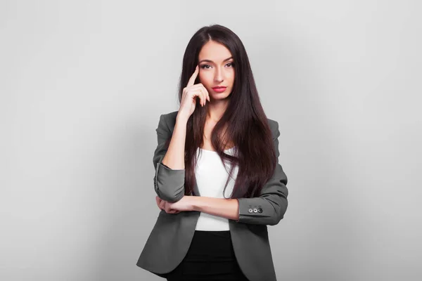 Mulher de negócios bonita com cabelo escuro, pensando em pé sobre um fundo cinza — Fotografia de Stock