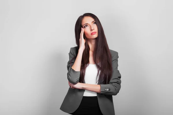 Vacker affärskvinna med mörkt hår, tänker stående på en grå bakgrund — Stockfoto
