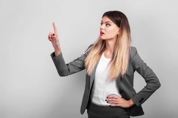 Leuke zakenvrouw toont uw product met haar hand op grijze achtergrond. — Stockfoto