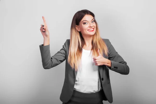 Nette Geschäftsfrau zeigt ihr Produkt mit der Hand auf grauem Hintergrund. — Stockfoto