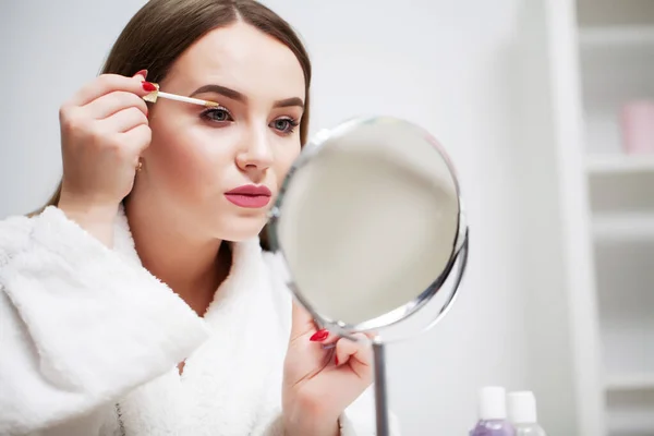 Chica bonita aplica maquillaje en su cara en el baño del hotel — Foto de Stock