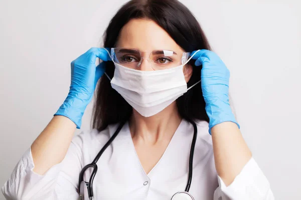 Médica com um casaco branco coloca uma máscara cirúrgica em seu rosto — Fotografia de Stock