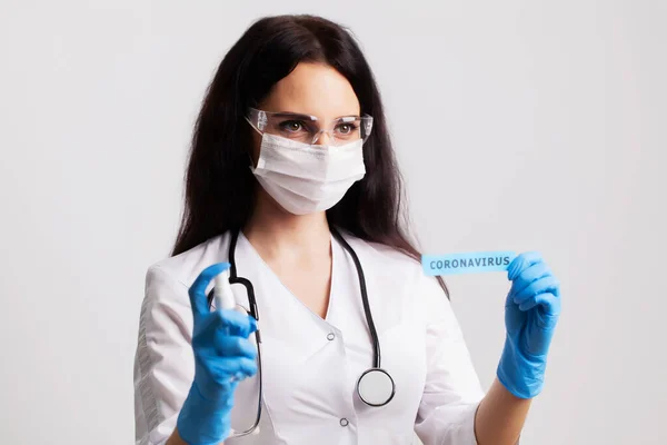 Médica em um casaco branco e máscara segurando a inscrição coronavírus — Fotografia de Stock