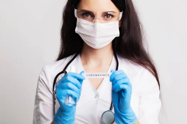 Médica em um casaco branco e máscara segurando a inscrição coronavírus — Fotografia de Stock