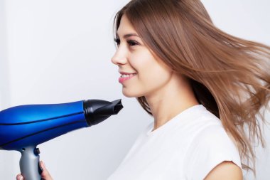 Güzel, genç bir manken saçına bakar, saçını kurutmak için saç kurutma makinesi kullanır.
