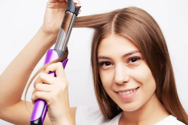 Linda jovem modelo feminino cuida de seu cabelo e usa um alisador de cabelo — Fotografia de Stock