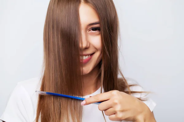 Schöne junge Frau kümmert sich um ihre Haare, kämmt lange Haare mit einem Kamm — Stockfoto